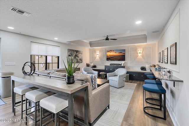 living room featuring crown molding, light hardwood / wood-style floors, a textured ceiling, and a tray ceiling