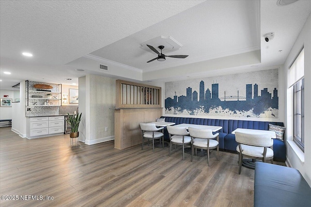 interior space featuring a wealth of natural light, wood-type flooring, white cabinetry, ornamental molding, and a tray ceiling