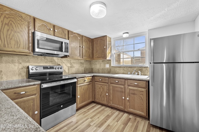 kitchen featuring stainless steel appliances, backsplash, a textured ceiling, light hardwood / wood-style flooring, and sink