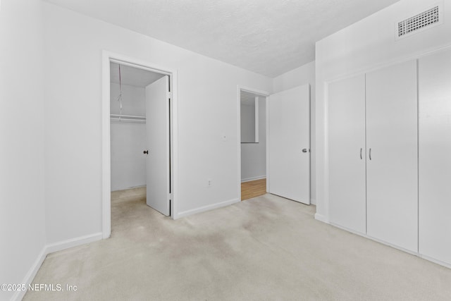 unfurnished bedroom featuring a textured ceiling, a closet, and light carpet