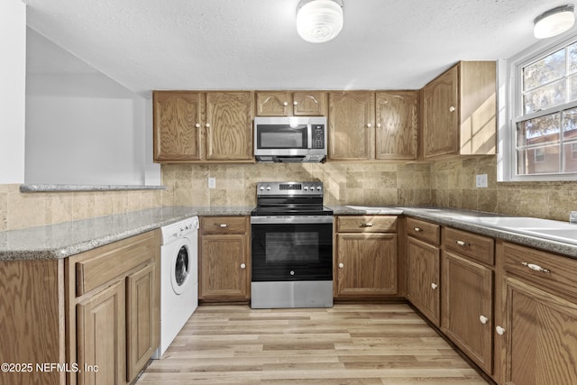 kitchen featuring washer / dryer, appliances with stainless steel finishes, light stone countertops, a textured ceiling, and light hardwood / wood-style flooring