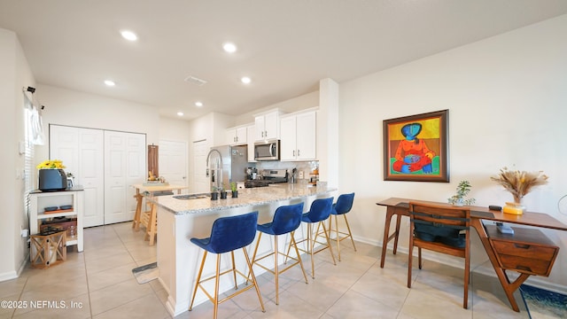 kitchen featuring light stone counters, stainless steel appliances, light tile patterned floors, a kitchen bar, and white cabinets