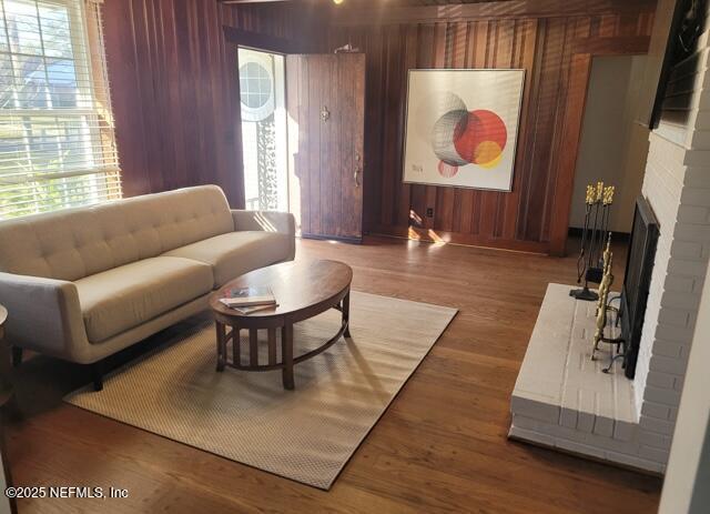 living room featuring wooden walls, a brick fireplace, and dark wood-type flooring