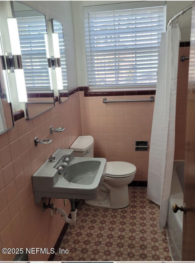 full bathroom featuring tile walls, shower / bath combo with shower curtain, toilet, and sink