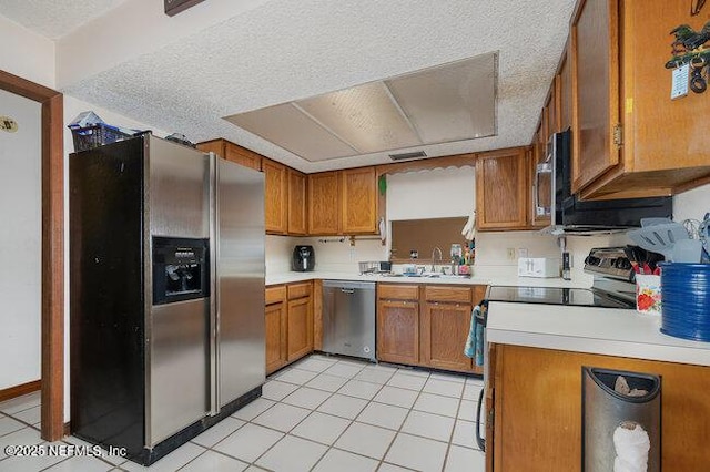 kitchen featuring appliances with stainless steel finishes, sink, light tile patterned floors, and a textured ceiling