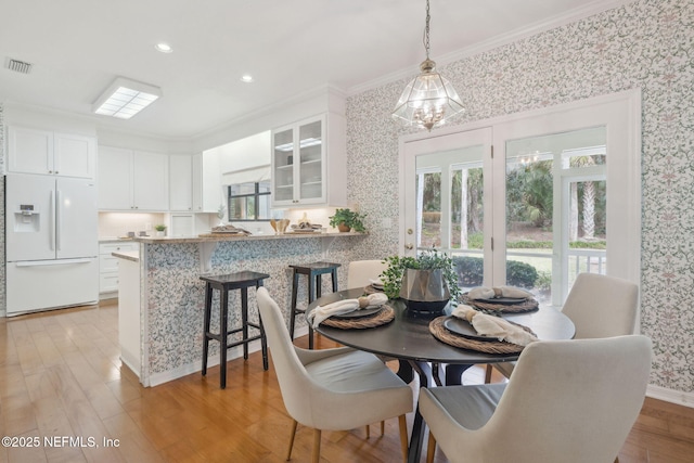 dining space featuring light wood-type flooring, wallpapered walls, visible vents, and crown molding