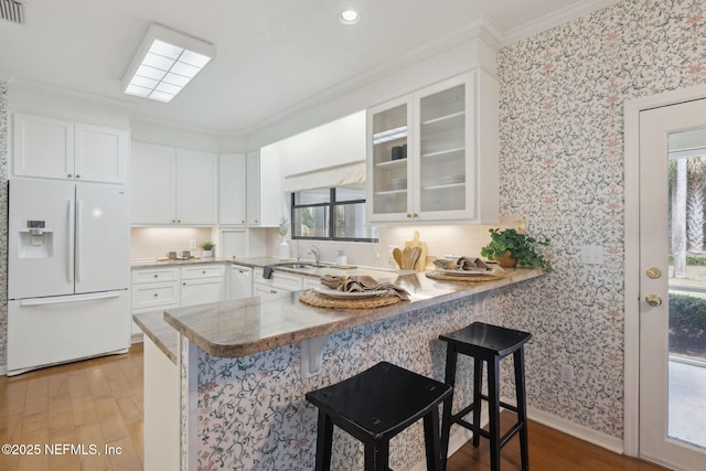 kitchen featuring white cabinetry, white refrigerator with ice dispenser, glass insert cabinets, and a breakfast bar area