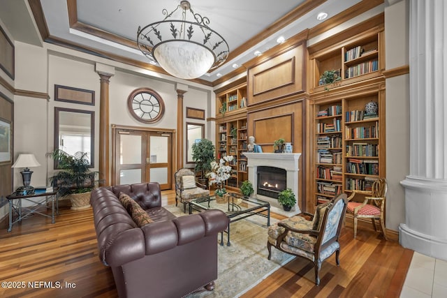 sitting room featuring decorative columns, wood-type flooring, ornamental molding, and built in features