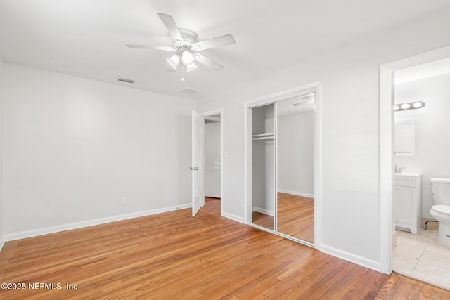 unfurnished bedroom featuring ensuite bathroom, a closet, ceiling fan, and light hardwood / wood-style flooring