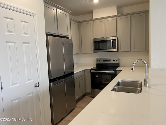 kitchen with sink, gray cabinets, a textured ceiling, appliances with stainless steel finishes, and light stone counters