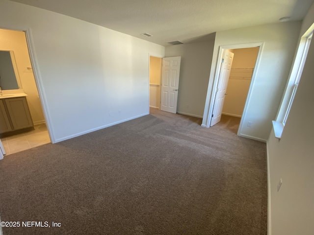 unfurnished bedroom featuring ensuite bath, a spacious closet, a closet, and light carpet