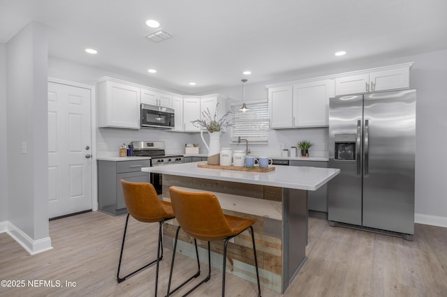 kitchen featuring visible vents, light wood-style flooring, a kitchen island, stainless steel appliances, and white cabinetry