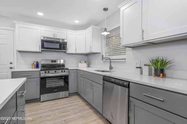 kitchen with light wood-style flooring, decorative light fixtures, gray cabinets, stainless steel appliances, and a sink