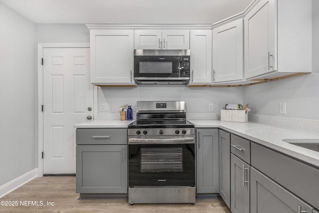 kitchen with light wood finished floors, stainless steel appliances, light countertops, gray cabinetry, and baseboards