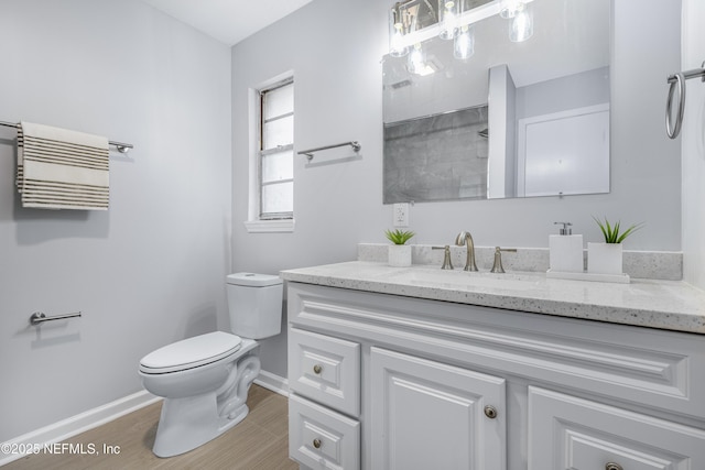 bathroom with wood finished floors, vanity, toilet, and baseboards