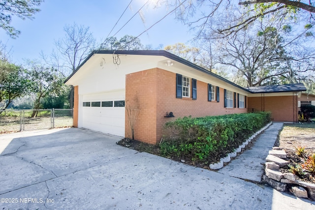 view of home's exterior with concrete driveway, an attached garage, a gate, fence, and brick siding