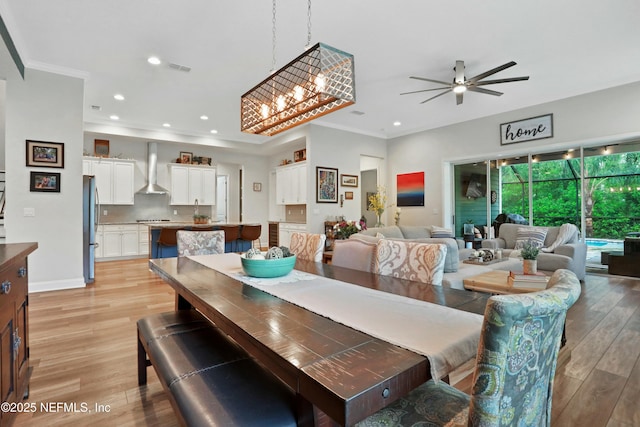 dining area with ceiling fan with notable chandelier, light wood-type flooring, and ornamental molding