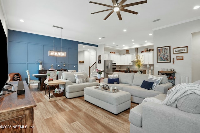 living room with light wood-type flooring, ceiling fan, and crown molding