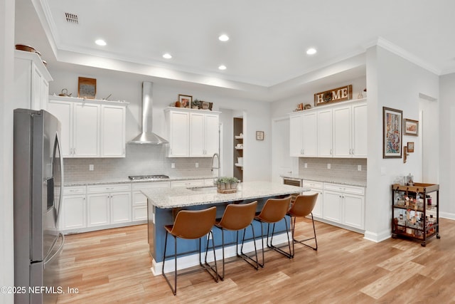 kitchen featuring stainless steel appliances, wall chimney range hood, a kitchen island with sink, and white cabinetry