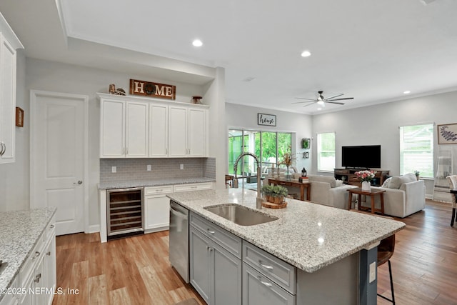 kitchen featuring stainless steel dishwasher, a center island with sink, wine cooler, white cabinetry, and sink