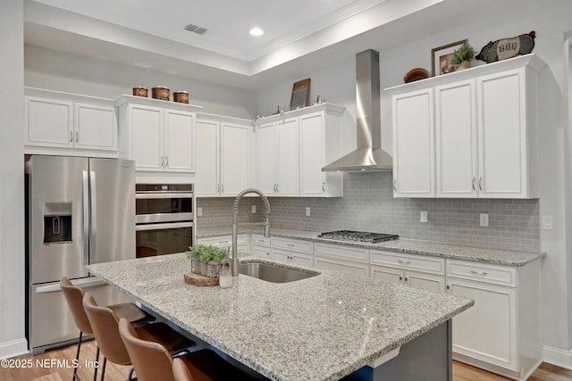 kitchen featuring sink, stainless steel appliances, wall chimney range hood, and light stone countertops