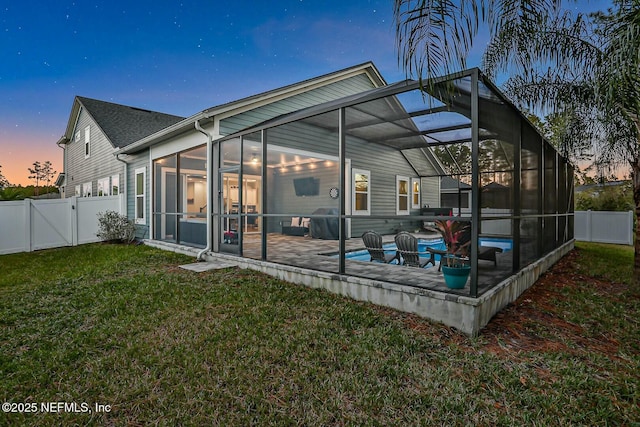 back house at dusk with a patio area, glass enclosure, a yard, and a fenced in pool