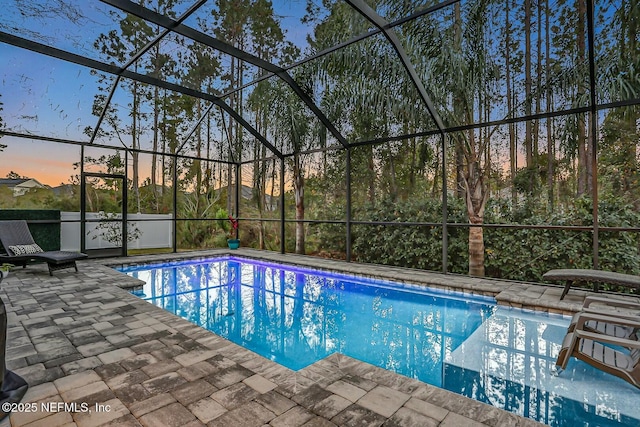 pool at dusk featuring a lanai and a patio