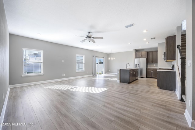 unfurnished living room with ceiling fan with notable chandelier, light hardwood / wood-style floors, and plenty of natural light