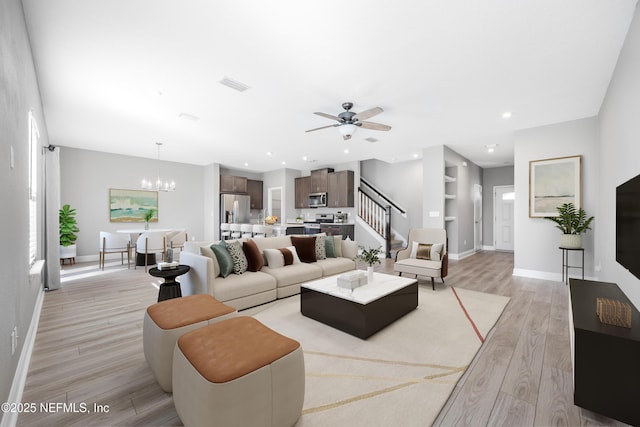 living room with ceiling fan with notable chandelier, built in features, and light hardwood / wood-style flooring