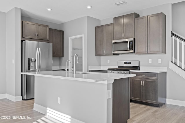 kitchen with sink, light hardwood / wood-style floors, an island with sink, dark brown cabinetry, and appliances with stainless steel finishes