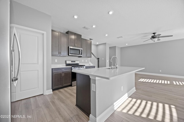 kitchen with light hardwood / wood-style floors, stainless steel appliances, an island with sink, ceiling fan, and sink