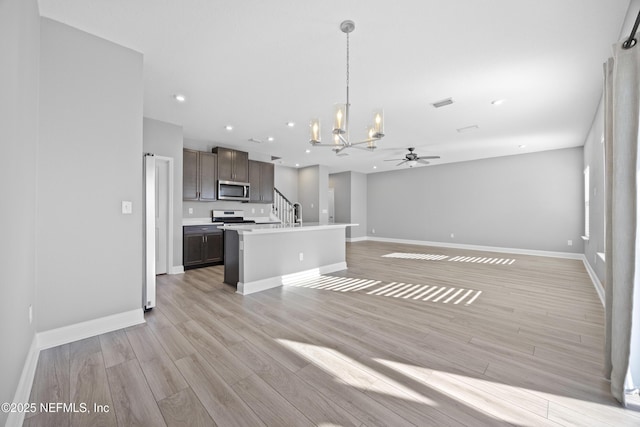 kitchen featuring stainless steel appliances, an island with sink, dark brown cabinets, pendant lighting, and light hardwood / wood-style flooring