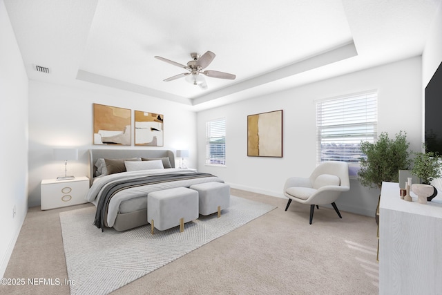 carpeted bedroom with a raised ceiling and ceiling fan