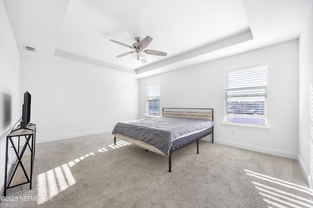 bedroom with a raised ceiling, light carpet, and ceiling fan