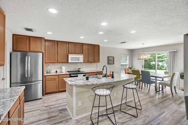 kitchen with decorative light fixtures, light stone counters, a kitchen bar, a kitchen island with sink, and appliances with stainless steel finishes