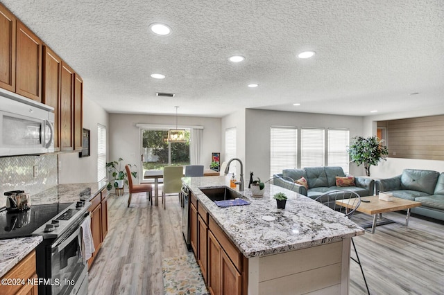 kitchen featuring sink, stainless steel appliances, a textured ceiling, hanging light fixtures, and a center island with sink