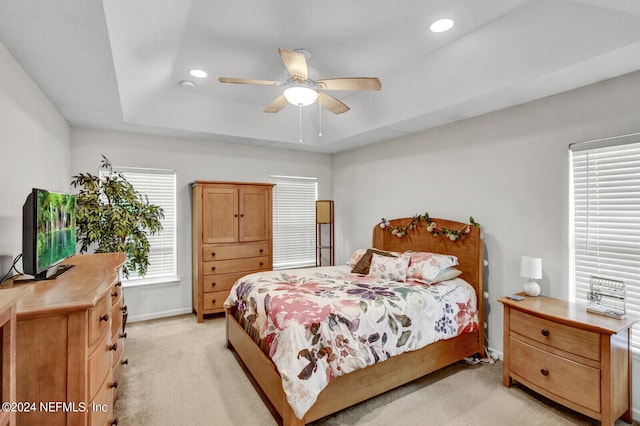 bedroom featuring ceiling fan, light colored carpet, and a tray ceiling