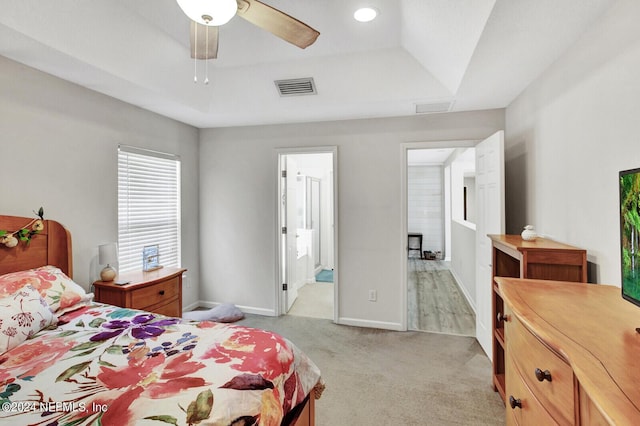 bedroom featuring ensuite bathroom, ceiling fan, a tray ceiling, and light carpet