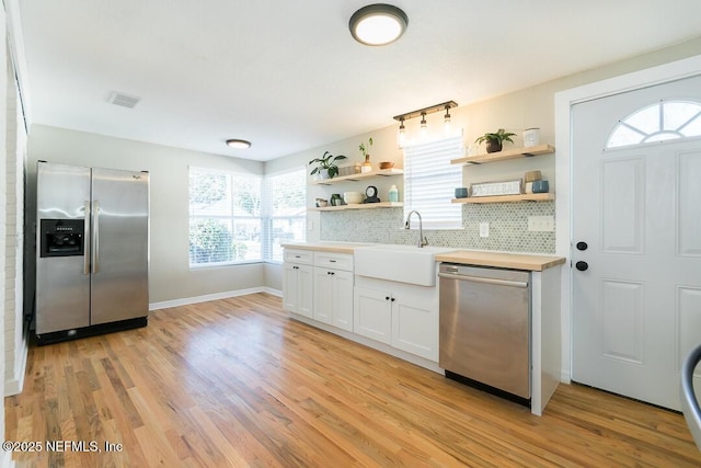 kitchen featuring white cabinetry, appliances with stainless steel finishes, sink, light hardwood / wood-style flooring, and tasteful backsplash