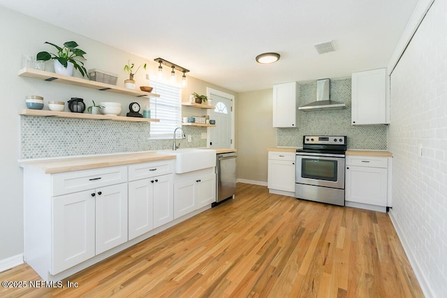 kitchen featuring sink, stainless steel appliances, white cabinetry, and wall chimney range hood