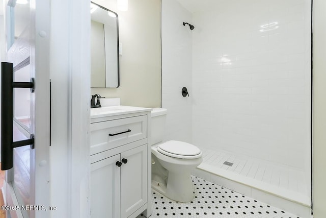 bathroom with tile patterned flooring, a tile shower, vanity, and toilet