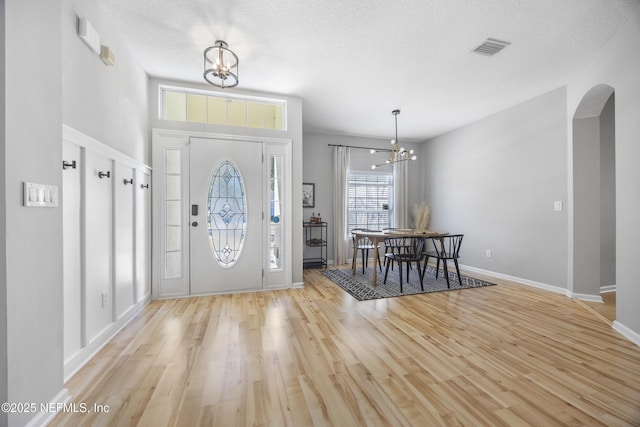 foyer with light wood-type flooring, a textured ceiling, and a notable chandelier