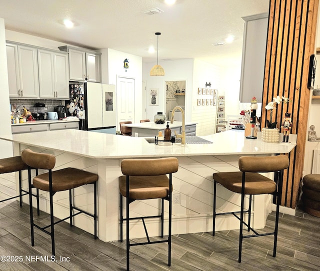 kitchen with decorative backsplash, a kitchen breakfast bar, sink, white fridge, and hanging light fixtures