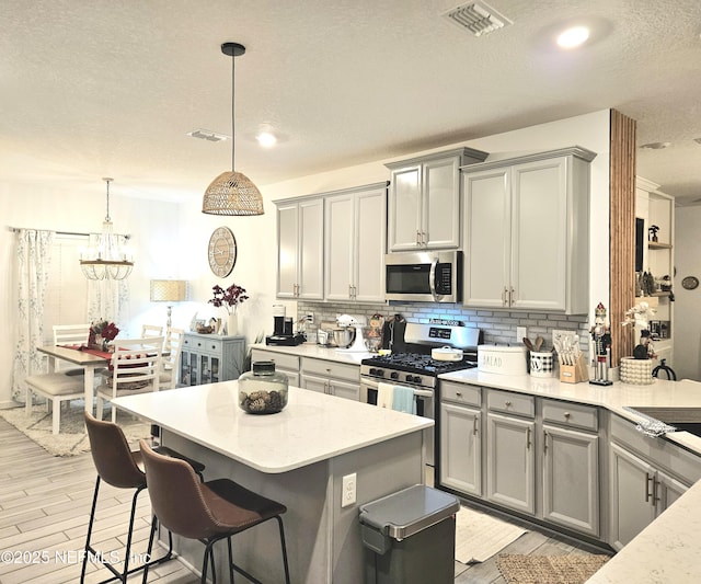 kitchen featuring decorative backsplash, appliances with stainless steel finishes, a textured ceiling, pendant lighting, and an inviting chandelier