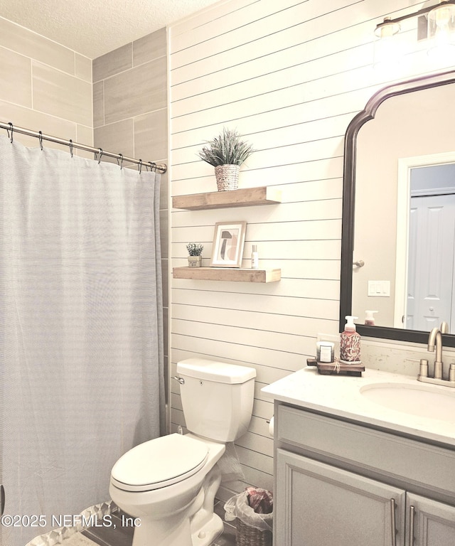 bathroom featuring vanity, wooden walls, toilet, a textured ceiling, and curtained shower