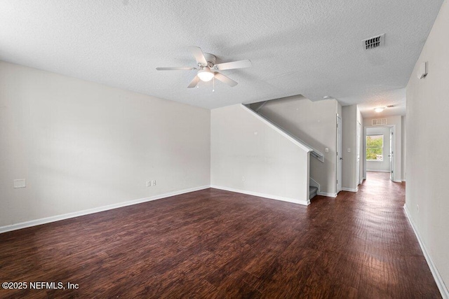 unfurnished living room featuring dark wood-style floors, visible vents, a textured ceiling, baseboards, and stairs