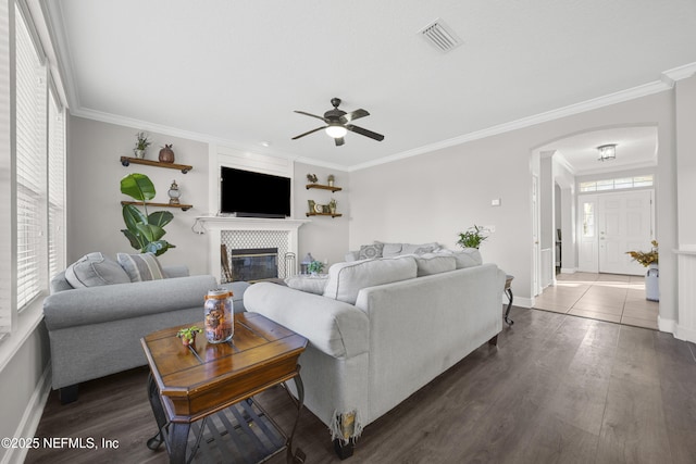 living room featuring ceiling fan, dark wood-type flooring, ornamental molding, and a fireplace