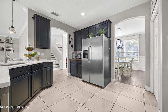 kitchen with stainless steel refrigerator with ice dispenser, light tile patterned flooring, hanging light fixtures, and sink