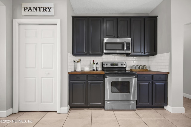 kitchen with backsplash, appliances with stainless steel finishes, light tile patterned flooring, and a textured ceiling