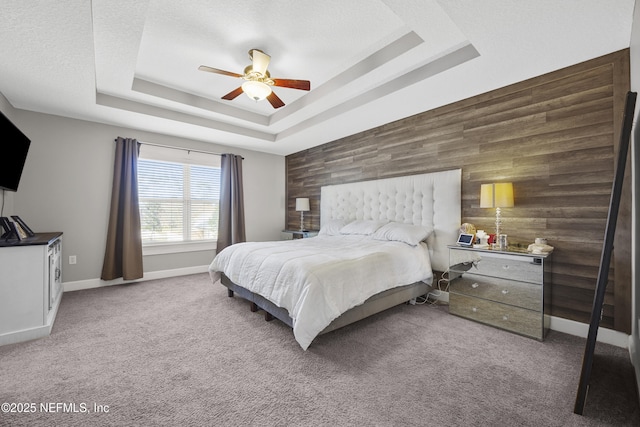 bedroom featuring ceiling fan, wooden walls, a tray ceiling, carpet flooring, and a textured ceiling